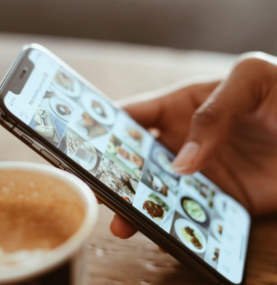 hand holding mobile phone next to coffee using social media aps